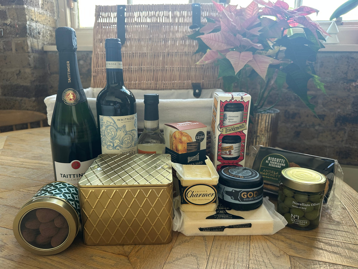 Gourmet gift basket with wine, cheese, and other snacks on a wooden table.