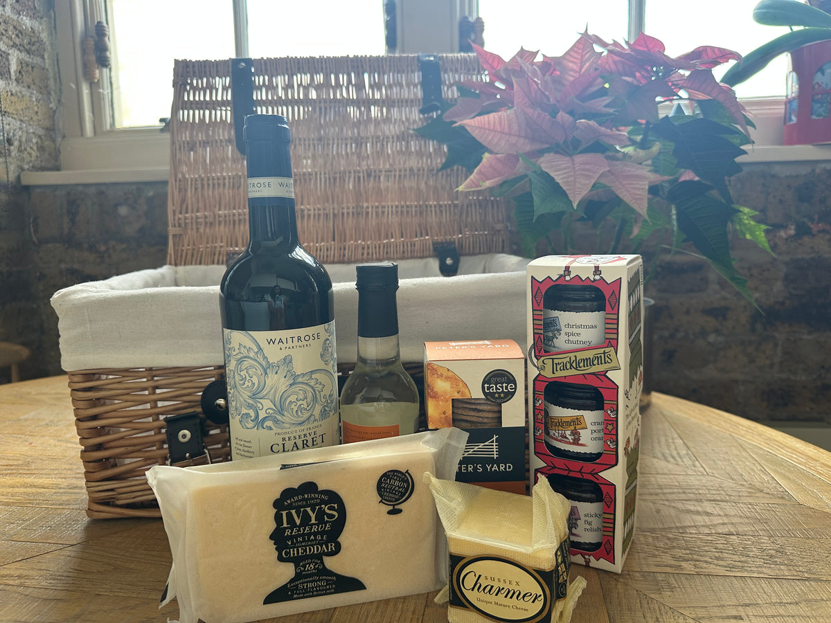 Gourmet gift basket with wine, cheese, and other items on a wooden table.